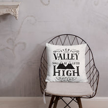 Load image into Gallery viewer, A monochrome square pillow sits on a wire framed chair against a pale grey textured wall. The pillow design is black on a white background, and reads &#39;Every valley shall be lifted high&#39; in a variety of typographic lettering, with flourishes and an illustration of two mountain peaks. 