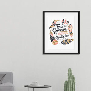 Artwork in a black frame featured in a room with hand drawn lettering reading "Tender Warriors Are Being Made Here" The words are in pink, navy and dark mustard yellow. 