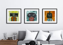 Load image into Gallery viewer, Three black frames on a wall above a grey sofa. The three frames have art prints of illustrated game controllers. The first frame features a vintage Nintendo controller, the second frame a Sega Genesis original controller, and the third frame is an Atari frame. 