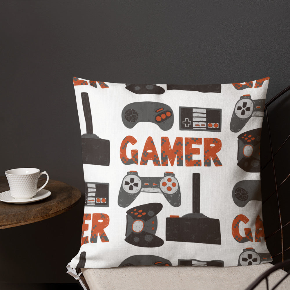A pillow on a chair with a coffee mug on a table next to it. The white pillow features hand drawn lettering and illustrations featuring different game controllers and the word 