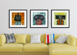Three black frames featuring a vintage Nintendo controller, the second frame a Sega Genesis original controller, and the third frame is an Atari frame. The frames are featured on a wall in a living room above a yellow sofa. 
