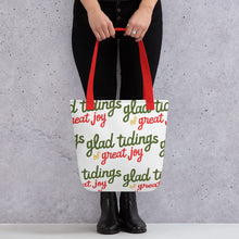 Load image into Gallery viewer, Someone holding a tote bag with red handles and a white fabric bag. The tote bag features the words &quot;glad tidings of great joy&quot; in green, yellow and red. 