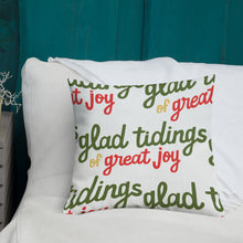Load image into Gallery viewer, A white pillow with illustrations leading on white bedding with a side table off to the side. The white pillow has the words &quot;glad tidings of great joy&quot; in a repeating pattern. The letters are in the colors green, red and yellow. 