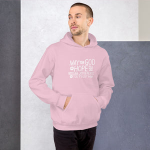 A man wearing a pink hoodie featuring hand drawn lettering in white with the words "May the God of hope fill you with all joy and peace as you trust him."