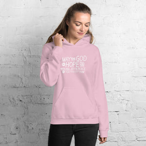 A woman wearing a pink hoodie featuring hand drawn lettering in white with the words "May the God of hope fill you with all joy and peace as you trust him."