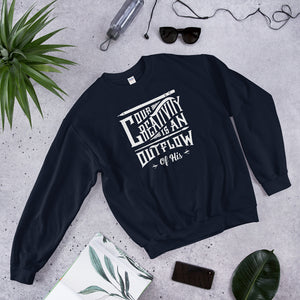 A navy sweatshirt laying on the ground with objects around it. The sweatshirt features hand drawn lettering in white with the words "Our creativity is an outflow of His."