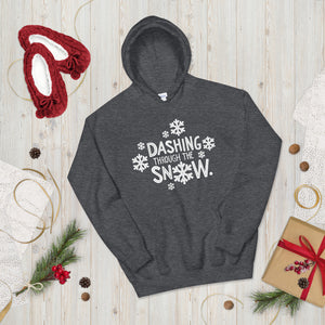 A hoodie laying on the ground with Christmas decorations and red slippers around it. The dark grey hoodie features the words Dashing through the snow in the middle in white. There are snowflake illustrations surrounding the words also in white. 