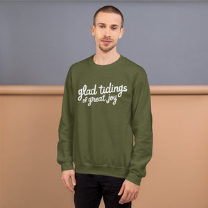 A man wearing a green sweatshirt featuring hand drawn lettering with the words "glad tidings of great joy" in white. 