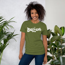 Load image into Gallery viewer, A woman wearing an olive green short sleeved t-shirt. The tee features lettering of the word &quot;Believe&quot; in white with the &quot;I&quot; of the word featured as an illustrated Christmas tree. 