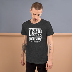 A man wearing a dark grey short sleeved t-shirt. The tee features hand drawn lettering featuring the words "Our creativity is an outflow of His" in white letters.  