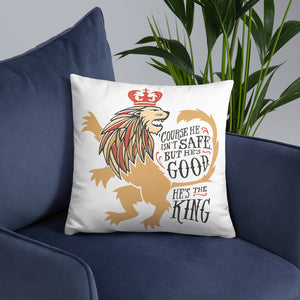 A white square pillow on a dark navy sofa. The artwork features hand drawn illustration of the Chronicles of Narnia lion character Aslan. Inside the illustration there is the quote "Course He Isn't Safe, But He's Good. He's the King."