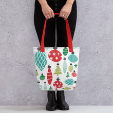 Load image into Gallery viewer, Someone holding a tote bag with red handles and a white fabric bag. The artwork features illustrated Christmas ornaments in the colors red, green and blue. 
