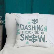Load image into Gallery viewer, A white pillow with illustrations leading on white bedding with a side table off to the side. The white pillow has the words &quot;Dashing through the snow&quot; in light and dark blue in a repeating pattern. Around the words are illustrated snowflakes. 