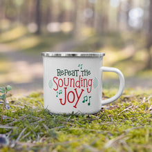 Load image into Gallery viewer, A white enamel mug with a silver enamel rim sitting in the grass. The illustrated design says &quot;Repeat the Sounding Joy&quot; in red and green letters. There are musical notes around the words. 