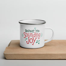 Load image into Gallery viewer, A white enamel mug sitting on top of a wood cutting board on a white background. The mug is white with the very top silver enamel. The design features the words &quot;Repeat the Sounding Joy&quot; in red and green with musical notes around the letters. 