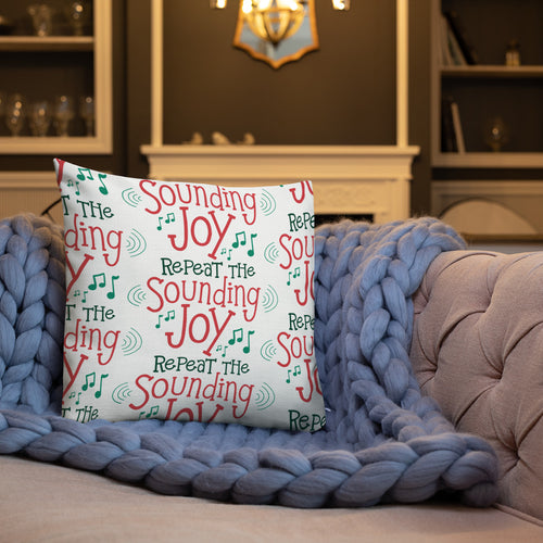 A white pillow on a sofa with a blue knitted blanket. The white pillow features the words 