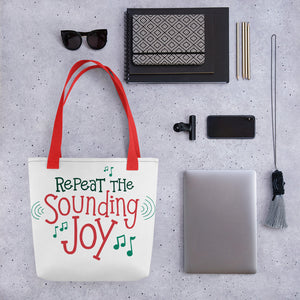A tote bag lying on a surface with a laptop and office items next to it. The tote bag has the song lyrics "Repeat the Sounding Joy" in red and green along with musical notes surrounding the lettering.  