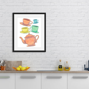 A black frame is on a white brick wall above a kitchen counter. The kitchen counter has some oils, a fruit basket and utensils on it. The frame has artwork on a white background with four teacups on saucers and one large teapot. The teacups are in muted colors of orange, blue, yellow and green and the teapot is a muted orange. On the teacups, saucers and teapot there is a light flower detail pattern.