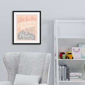A pink print hanging on a pale grey wall, over a grey armchair and white bookshelves. The print reads 'Let her sleep for when she wakes she will move mountains' in a pink, white, and light grey lettering design, with a grey mountain illustration at the bottom.