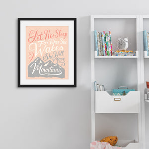 A pink print hanging on a pale grey wall, next to white bookshelves. The print reads 'Let her sleep for when she wakes she will move mountains' in a pink, white, and light grey lettering design, with a grey mountain illustration at the bottom.