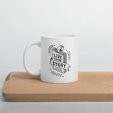 Load image into Gallery viewer, A white mug sitting on a light wood cutting board. The design features the words &quot;Live Your Story&quot; with the words inside an illustrated book. 