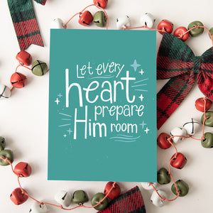 A Christmas card featured on top of some red and white Christmas decorations. The card background color is teal with white lettering reading "Let every heart prepare him room" with stars and lines around the words.