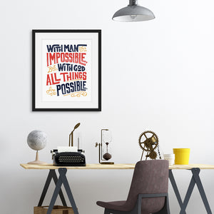 A black frame above a desk with artwork printed on white paper. The artwork features hand drawn lettering with the Matthew 19:26 Bible verse reading "With man this is impossible but with God all things are possible."  The lettering is in navy, red and mustard yellow. 