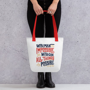 Someone holding a tote bag with red handles and a white fabric bag. The artwork features the Matthew 19:26 Bible verse reading "With man this is impossible but with God all things are possible." The lettering is in navy, red and mustard yellow.
