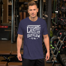 Load image into Gallery viewer, A man wearing a heather midnight blue color short sleeved t-shirt. The t-shirt features hand drawn lettering in white with the words &quot;Our creativity is an outflow of His.&quot;