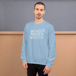 A man wearing a light blue sweatshirt featuring hand drawn lettering in white with the words "May the God of hope fill you with all joy and peace as you trust him."