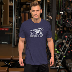 A man wearing a heather midnight blue color short sleeved t-shirt. The t-shirt features hand drawn lettering in white with the words "May the God of hope fill you with all joy and peace as you trust him."