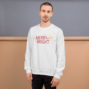 A man wearing a white sweatshirt featuring hand drawn lettering in red with the words Merry and Bright. Around the words are yellow illustrated stars. 
