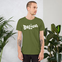 Load image into Gallery viewer, A man wearing an olive green short sleeved t-shirt. The tee features lettering of the word &quot;Believe&quot; in white with the &quot;I&quot; of the word featured as an illustrated Christmas tree. 