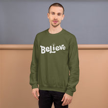 Load image into Gallery viewer, A man wearing a hunter green sweatshirt featuring hand drawn lettering with the word Believe. The &quot;I&quot; of the word Believe is an illustrated Christmas tree. 