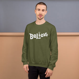 A man wearing a hunter green sweatshirt featuring hand drawn lettering with the word Believe. The "I" of the word Believe is an illustrated Christmas tree. 