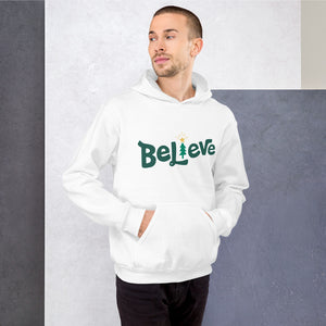 A man wearing a white hoodie featuring hand drawn lettering in green with the word "Believe." The "I" of Believe is a Christmas tree illustration.