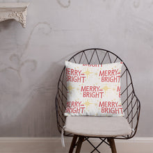Load image into Gallery viewer, The pillow is leaning on a metal chair with a cushion. The white pillow features a Christmas pattern of yellow illustrated stars and the red words of Merry and Bright. 