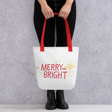 Load image into Gallery viewer, Someone holding a tote bag with red handles and a white fabric bag. The artwork features an illustrated Christmas pattern with yellow stars and the words Merry and Bright in red. 