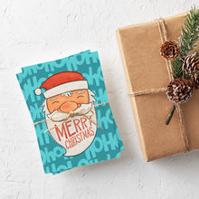 Load image into Gallery viewer, A stack of Christmas cards with brown string wrapped around them. A brown craft paper gift is off to the side. The card has a blue background with the words &#39;ho ho ho&#39; in a lighter shade of blue. On top of the background is an illustrated Santa Claus with the words &quot;Merry Christmas&quot; in his beard.