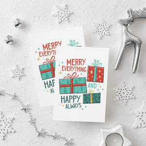 Two Christmas cards laying on a white background with white and silver Christmas decorations on the table. The card has a white background with the words "Merry Everything and Happy Always." There are three illustrated Christmas gifts in light red, green and blue with patterns on them.