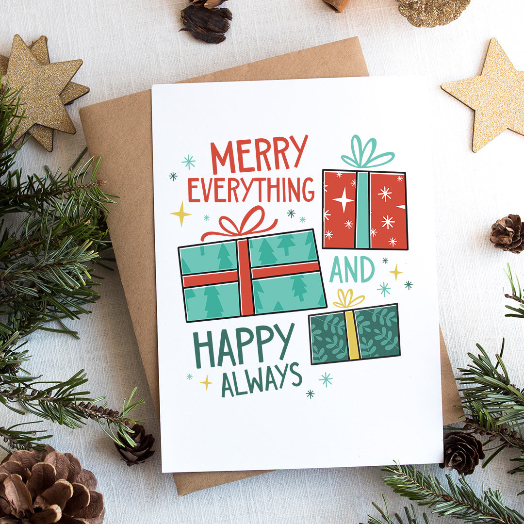 A photo of a Christmas card on top of a brown paper wrapped gift with Christmas decor around it. The card has a white background with the words 