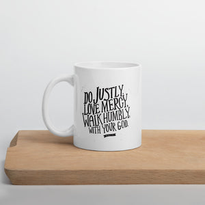 A white mug with black lettering with the words Do justly, love mercy, walk humbly, with your God, Micah 6:8.