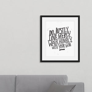 Framed artwork in a black frame on a wall above a sofa featuring a white paper print with black lettering featuring the Bible verse “Do justly, love mercy, walk humbly, with your God, Micah 6:8.”