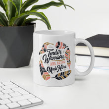 Load image into Gallery viewer, A mug featured on a desk with a plant and a keyboard. The white mug features hand drawn lettering with the words &quot;Tender Warriors Are Being Made Here&quot; The words are in pink, navy and dark mustard yellow. 