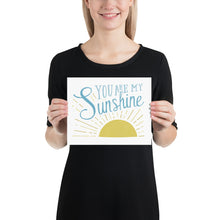Load image into Gallery viewer, A smiling woman holds up a small print. The print reads &#39;You are my sunshine&#39; in blue lettering, over a yellow sun illustration.