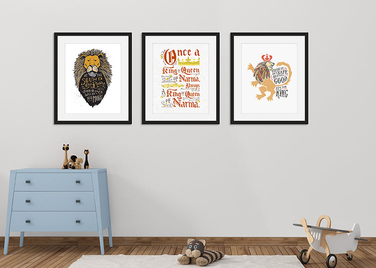 Three black frames with quote illustrations featured on a wall in a nursery. Frame one features a lion's head illustration of Aslan with the quote 