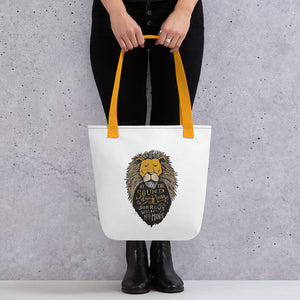 A woman holding a tote bag with black pants and black shoes on. The tote bag has mustard yellow handles and is white. The artwork on the bag is of Aslan with the words ""At the sound of his roar sorrows will be no more."