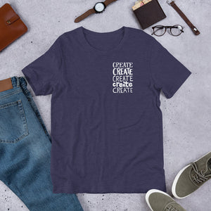 A short sleeved T-shirt laying flat with objects around it. The tee is in the color heather midnight navy blue with the words "create, create, create, create, create" in white in a small rectangle on the upper left side. 