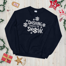 Load image into Gallery viewer, A navy blue sweatshirt laying on a table with Christmas objects around it. The sweatshirt has the words &quot;Dashing through the snow&quot; in white. There are snowflakes around the letters. 