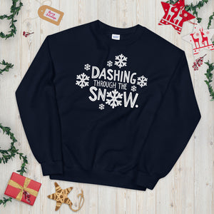 A navy blue sweatshirt laying on a table with Christmas objects around it. The sweatshirt has the words "Dashing through the snow" in white. There are snowflakes around the letters. 